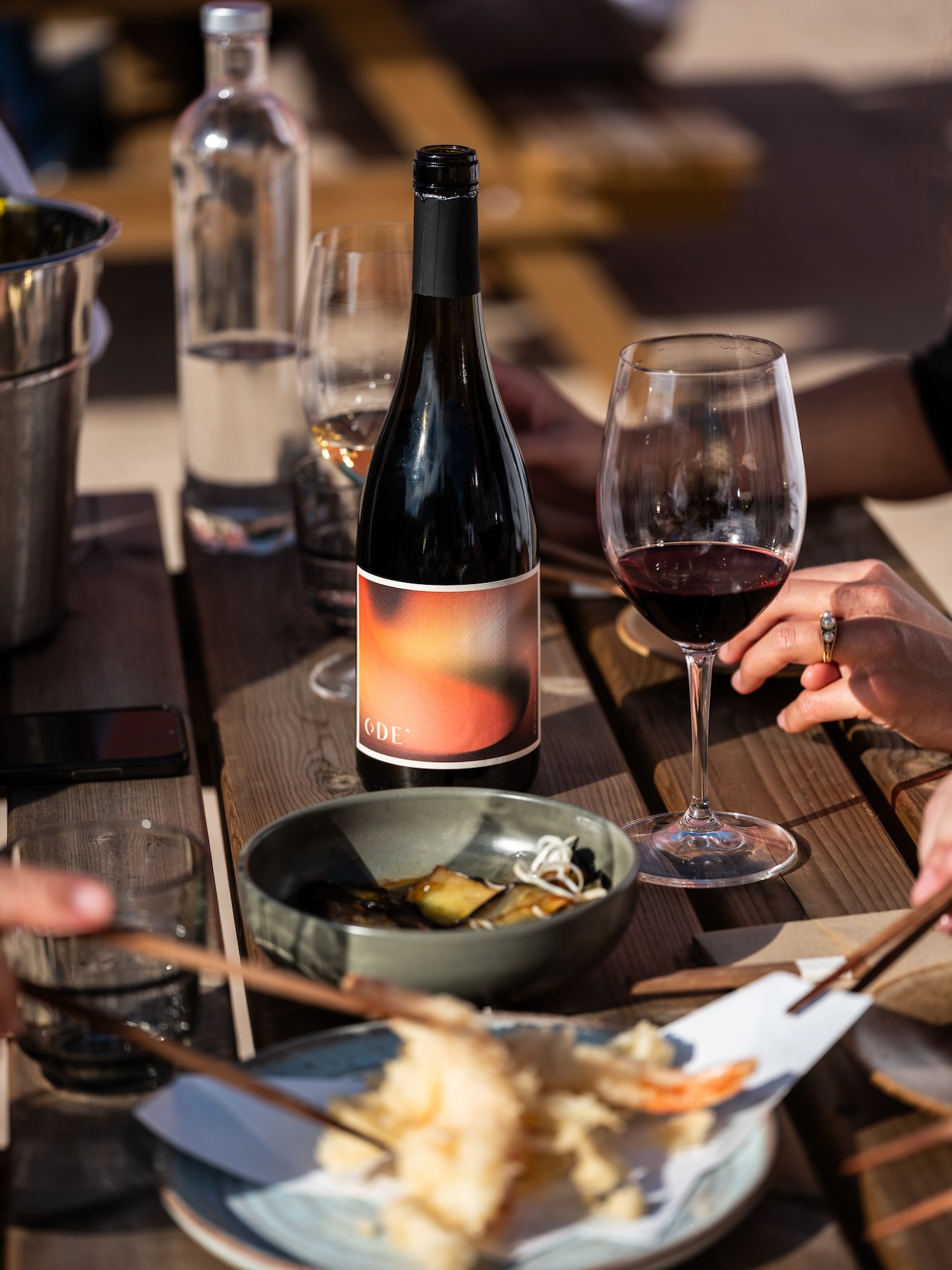 A table at the Ode Cellar Door restaurant, with a bottle of Ode red wine, glasses of wine, and shared plates in the evening light.