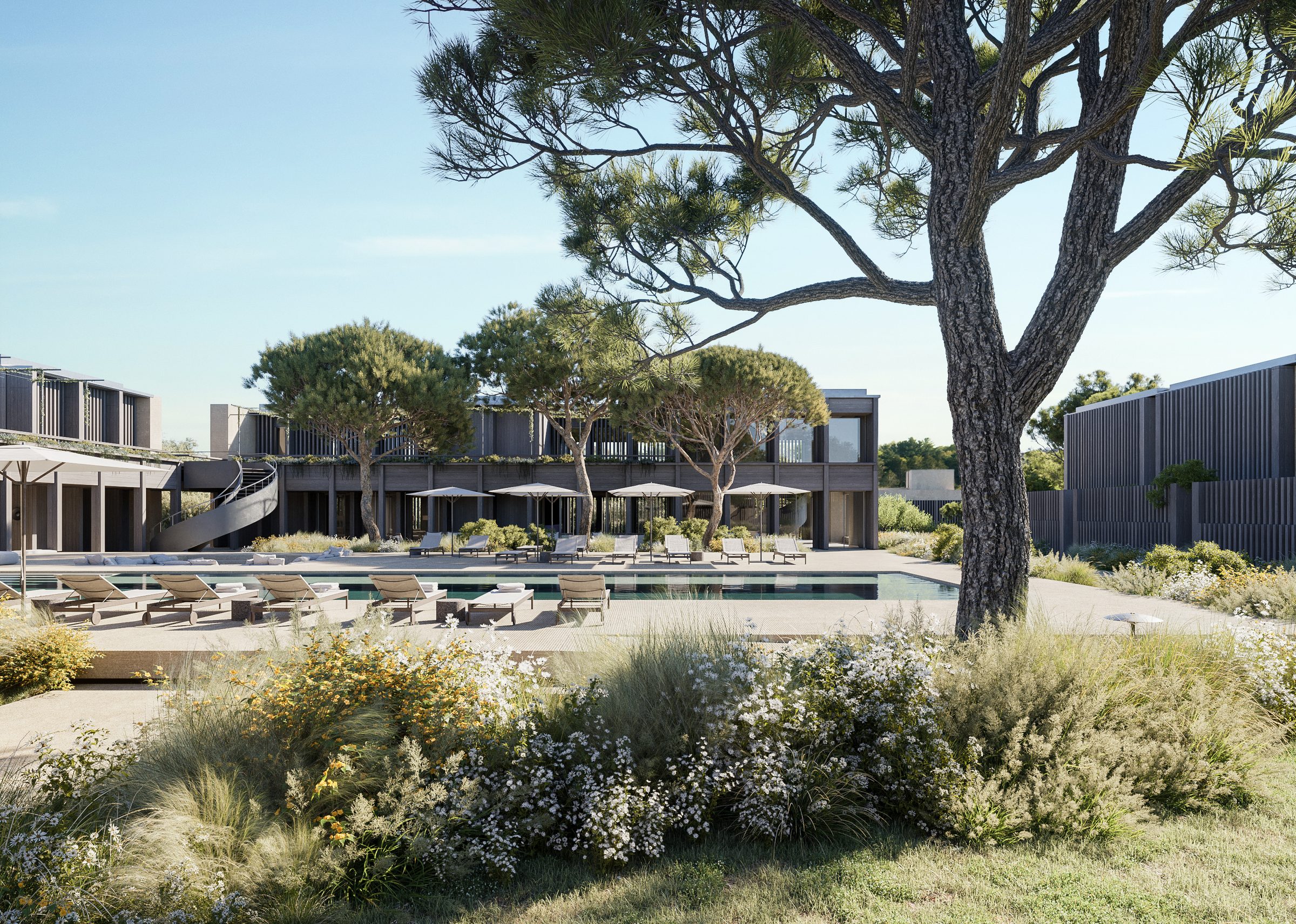 The full pool courtyard at the AMAIA hotel — a long rectangular pool, sunken seating, sun loungers, and the colonnaded restaurant beyond.